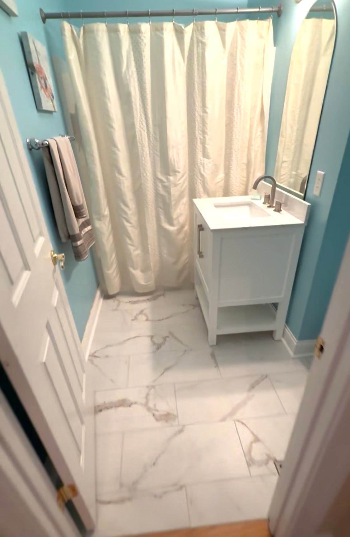 White marble-look porcelain tile in a bathroom with teal walls.