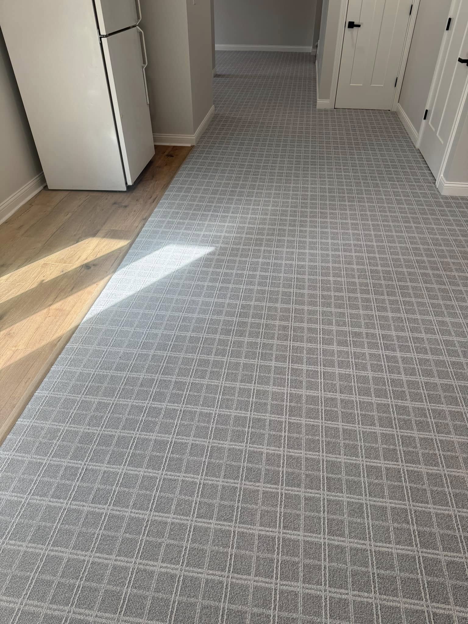 Gray plaid-patterned carpet in a hallway, transitioning to hardwood flooring by the kitchen.